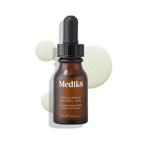 A dark amber dropper bottle labeled "Medik8 Intelligent Retinol™" is set against light green droplets, emphasizing this vitamin A serum's age-defying power.