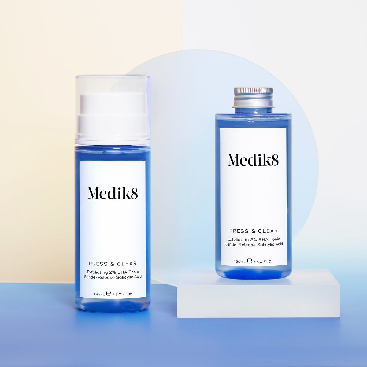 Two Medik8 Press & Clear bottles sit on a blue and beige background, featuring one with a pump for BHA toning and another with a screw cap, both enriched with Salicylic Acid.