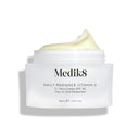 A jar of Medik8 Daily Radiance Vitamin C™ cream with an open lid shows its light, creamy texture. The label promotes it as a dual-purpose moisturizer providing antioxidant protection and SPF 30 for vibrant, shielded skin.