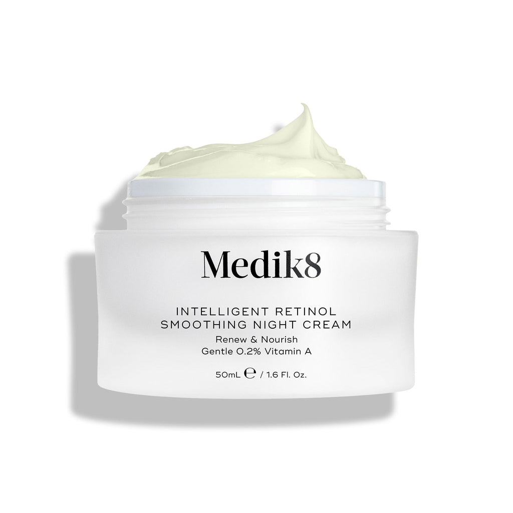 A jar of Medik8 Intelligent Retinol® Smoothing Night Cream, featuring 0.2% vitamin A, is displayed with the lid off, revealing the luxurious cream inside. This anti-aging moisturizer promises overnight complexion renewal for a youthful glow.