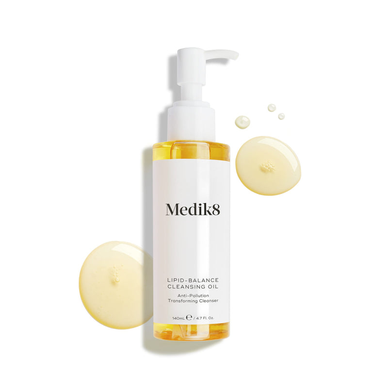 A bottle of Lipid-Balance Cleansing Oil™ by Medik8, surrounded by oil droplets. The 140ml (4.7 fl. oz) bottle with a pump features innovative anti-pollution technology, effortlessly removing makeup while nourishing your skin.