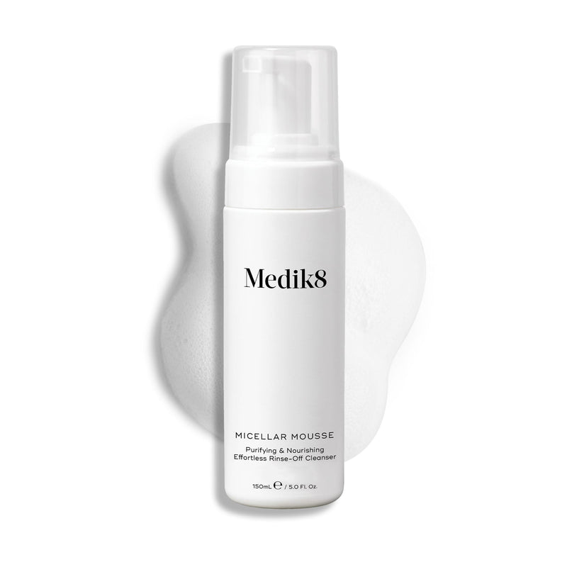 A white bottle of Medik8's Micellar Mousse™, featuring micellar cleansing technology, rests against a white foam backdrop. The label reads: "Purifying & Nourishing, Effortless Rinse-Off Cleanser." Ideal for makeup removal, the bottle holds 150 ml (5 fl oz).