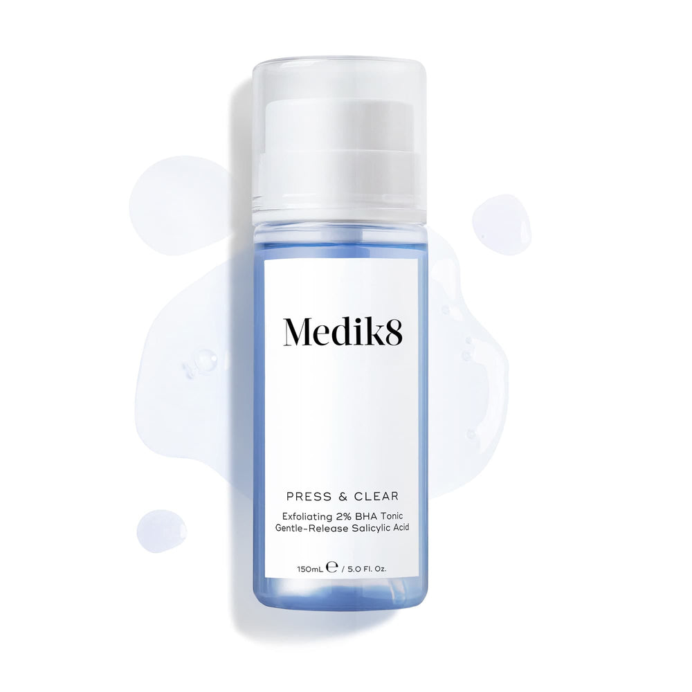 Clear bottle of Medik8's Press & Clear™ BHA Tonic features a white label, set against a backdrop of spilled liquid. Perfect for blemish-prone skin, this exfoliating toner helps achieve clearer skin effortlessly.