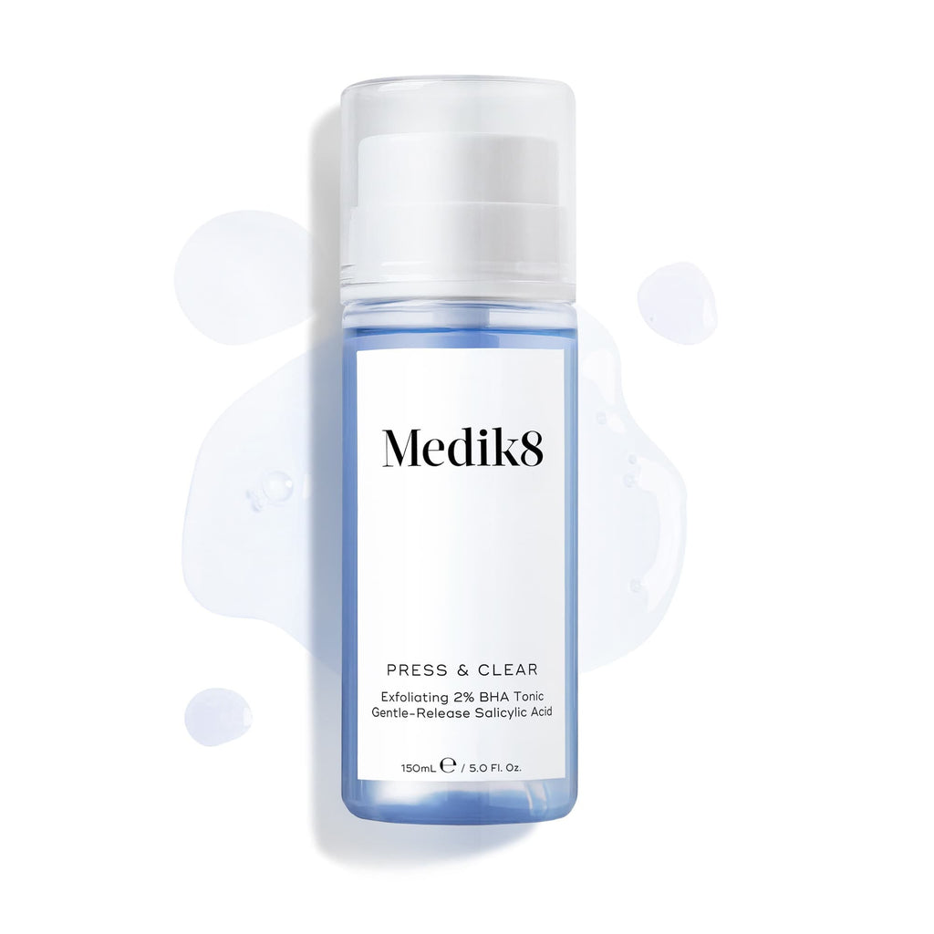 Clear bottle of Medik8's Press & Clear™ BHA Tonic features a white label, set against a backdrop of spilled liquid. Perfect for blemish-prone skin, this exfoliating toner helps achieve clearer skin effortlessly.