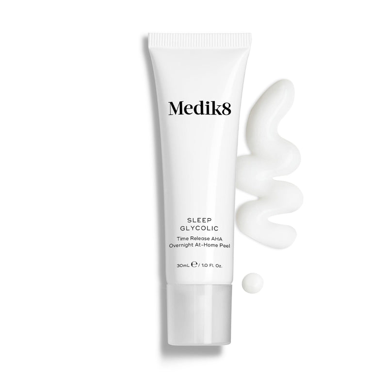 A white tube labeled "Sleep Glycolic™" by Medik8, featuring glycolic acid for skin revitalization, is set against a plain background with white cream gently oozing beside it.