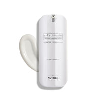 A white bottle of Medik8 r-Retinoate® Day & Night cream, containing retinyl retinoate and vitamin A, comes with a pump dispenser and is pictured next to a swirl of the anti-aging serum.