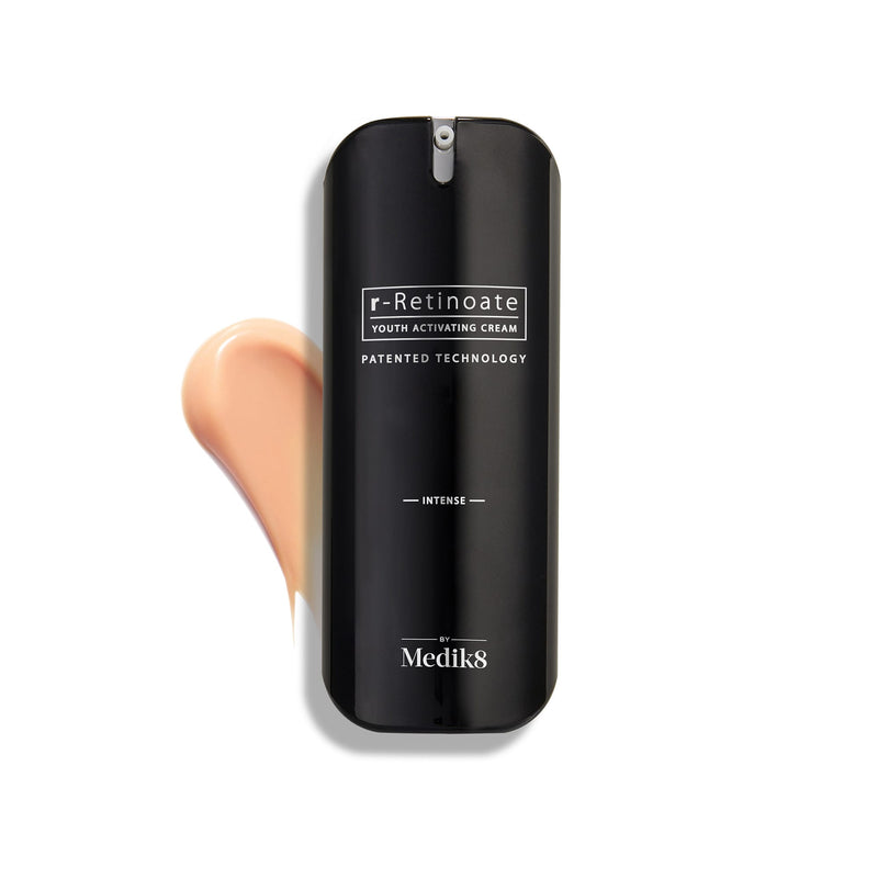A sleek black bottle of Medik8 r-Retinoate® Intense, enriched with Vitamin A for potent wrinkle reduction, rests beside a luxurious cream smear on a pristine white background.