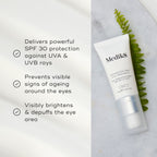A tube of Medik8's Advanced Day Eye Protect™ cream is on a marble surface next to a leaf, highlighting its SPF 30 protection, anti-aging properties, and brightening effects for effective wrinkle prevention.