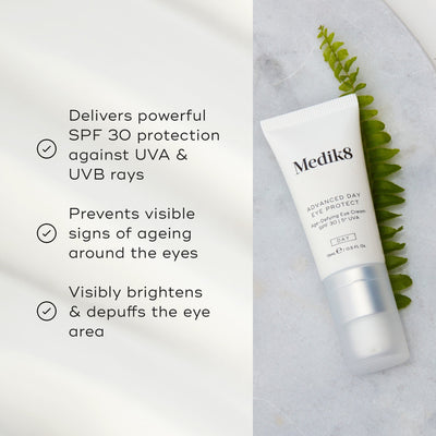 A tube of Medik8's Advanced Day Eye Protect™ cream is on a marble surface next to a leaf, highlighting its SPF 30 protection, anti-aging properties, and brightening effects for effective wrinkle prevention.