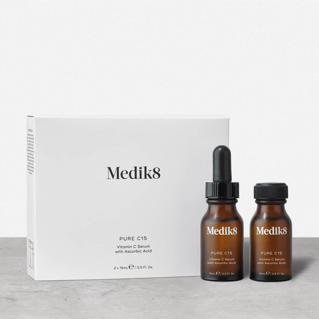 Two brown bottles labeled "Pure C15™" from Medik8, featuring white and orange text, are placed in front of a white box labeled "Pure C15 Vitamin C Serum with Ascorbic Acid." This age-defying serum provides antioxidant protection for rejuvenating your skin.