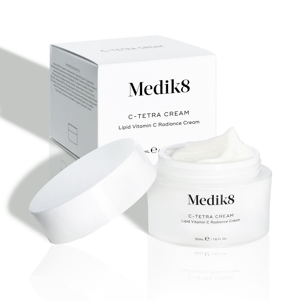 An open jar of Medik8's C-Tetra® Cream, displayed in front of its box, reveals a smooth white cream enriched with vitamin C.