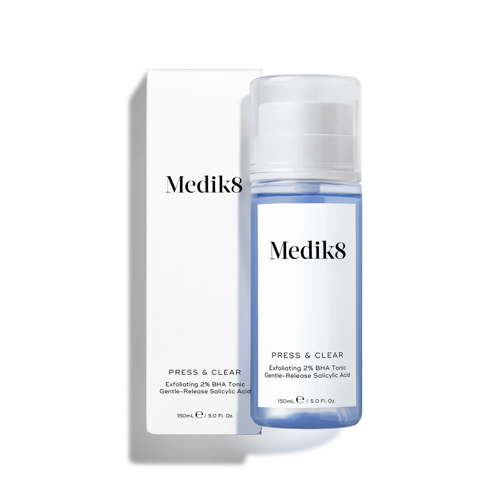 A bottle of Medik8's Press & Clear™ is shown next to its white packaging. The clear bottle reveals a blue liquid designed for blemish-prone skin, functioning as a BHA toner to help achieve clearer skin.
