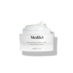 A small white jar labeled "Advanced Night Eye™" by Medik8 reveals its rejuvenating nighttime eye cream, rich in vitamin A, with the lid off and cream visible.