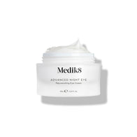 A small white jar labeled "Advanced Night Eye™" by Medik8 reveals its rejuvenating nighttime eye cream, rich in vitamin A, with the lid off and cream visible.