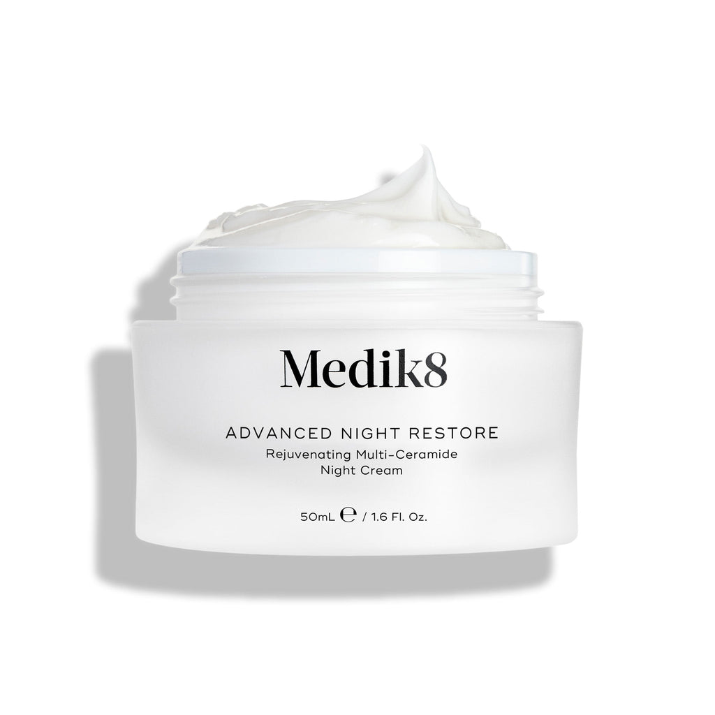A 50mL jar of Medik8's Advanced Night Restore™, with the lid off, reveals its ceramide-rich formula. This rejuvenating night cream highlights a luxurious white texture and visible plumping effects.