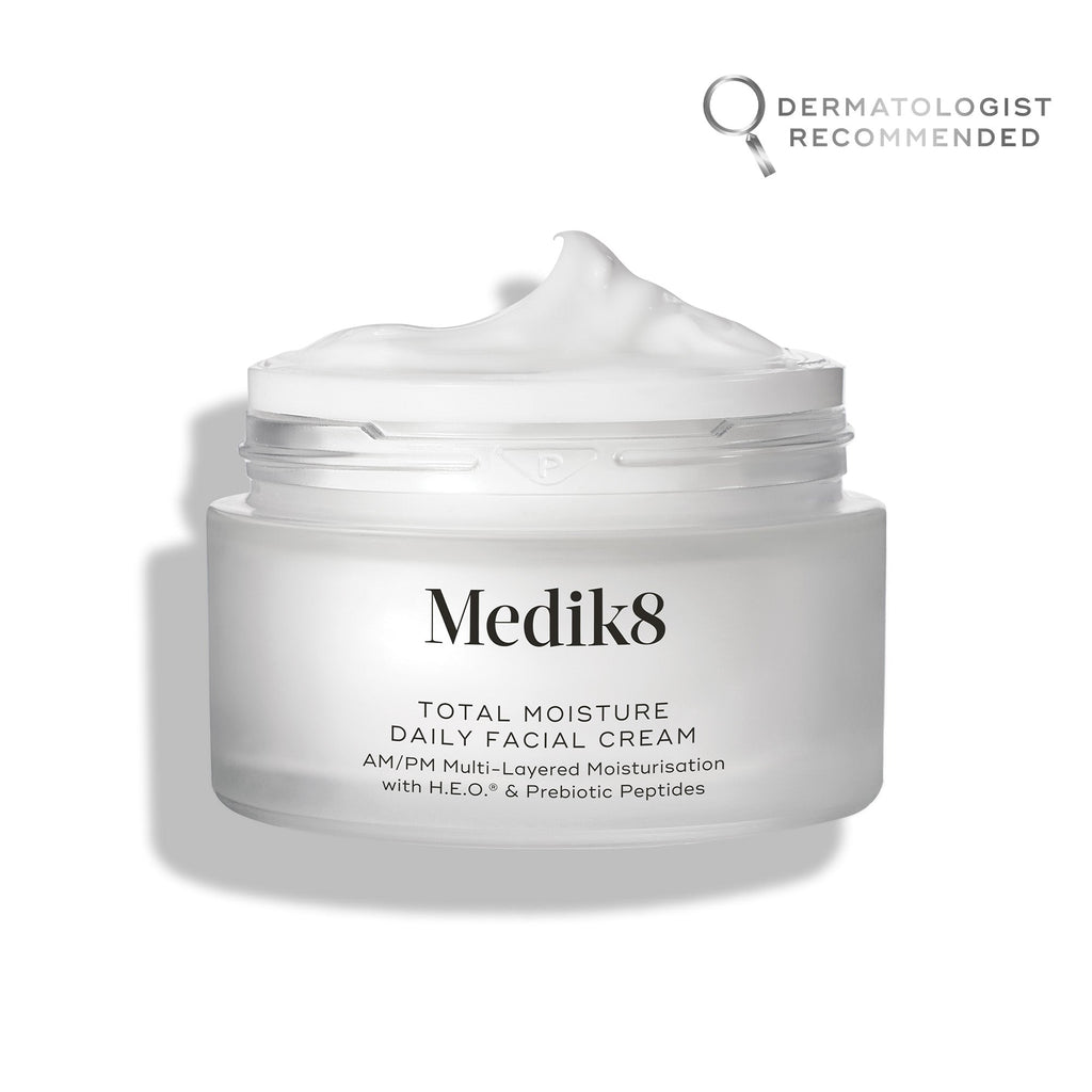 An open jar of Medik8's Total Moisture Daily Facial Cream™ shows its creamy contents for deep hydration. The label endorses AM/PM use and includes prebiotic peptides for microbiome support, with a "dermatologist recommended" badge prominently visible.