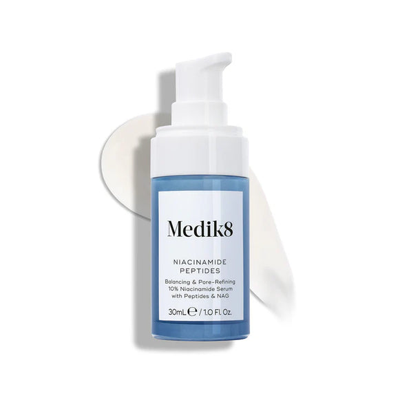 A blue and white pump bottle labeled "Niacinamide Peptides" by Medik8 Cyprus stands before a smear of white serum, showcasing this non-comedogenic, pore-refining skincare product.-81