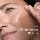 A close-up of a woman's face with Medik8 Cyprus Exo-PDRN Prismatic+ applied to her cheek, accompanied by the text "For Full-Spectrum Results.