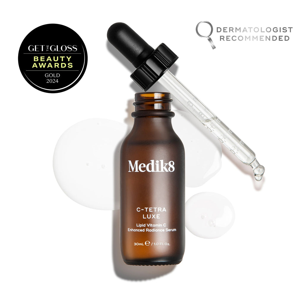 A brown bottle of Medik8 C-Tetra® Luxe serum with a dropper, liquid drops, an award badge, and "Dermatologist Recommended" text on a white background—formulated with vitamin C to enhance radiance and target fine lines.