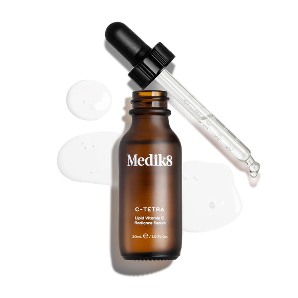 A brown bottle labeled "C-Tetra®" by Medik8, with a black dropper, is displayed on a white background alongside clear liquid drops. This vitamin C-rich antioxidant serum enhances skin radiance.-6