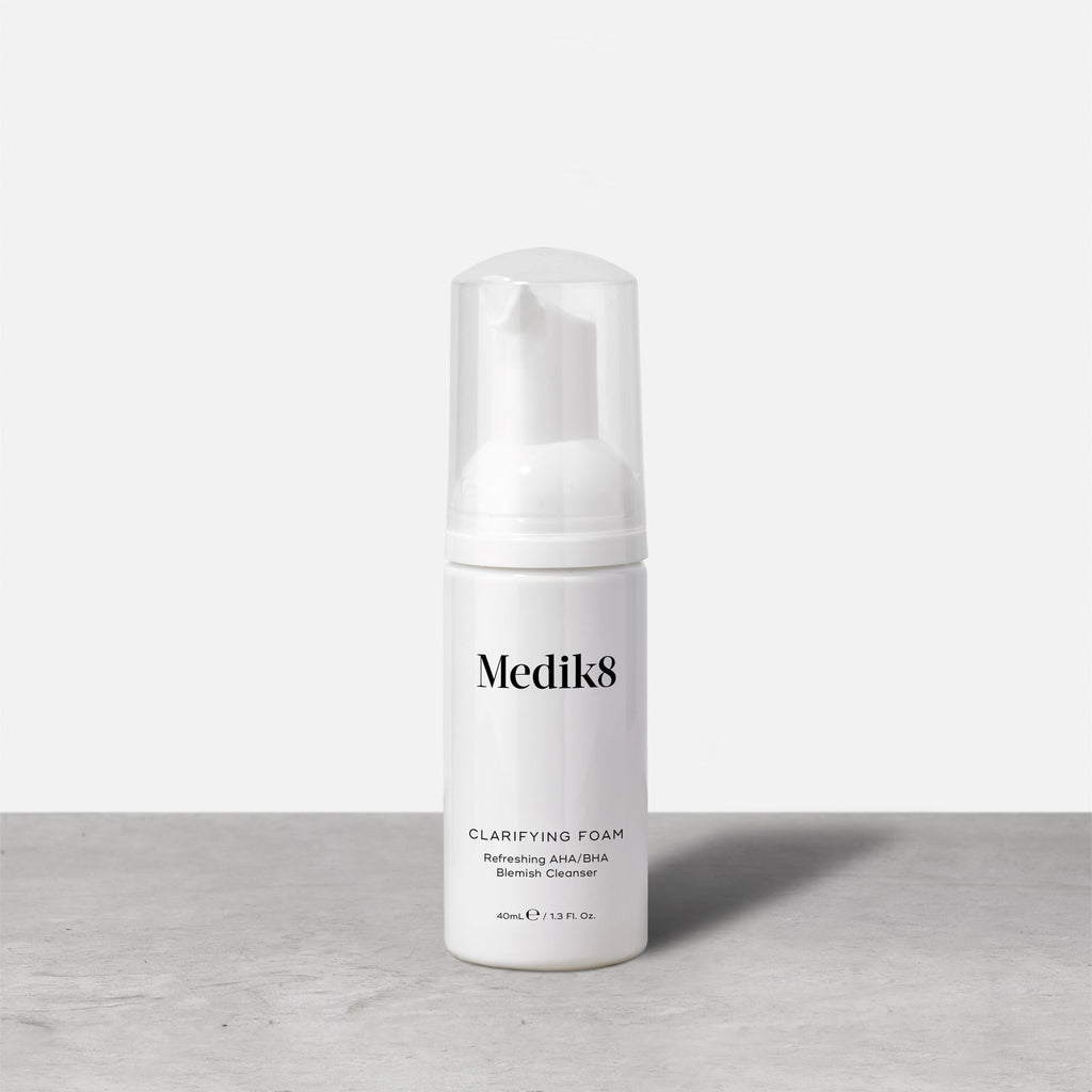 A Medik8 Clarifying Foam™ Blemish Cleanser in a white bottle with powerful AHAs and BHAs has a clear cap, set on a gray surface against a white background.