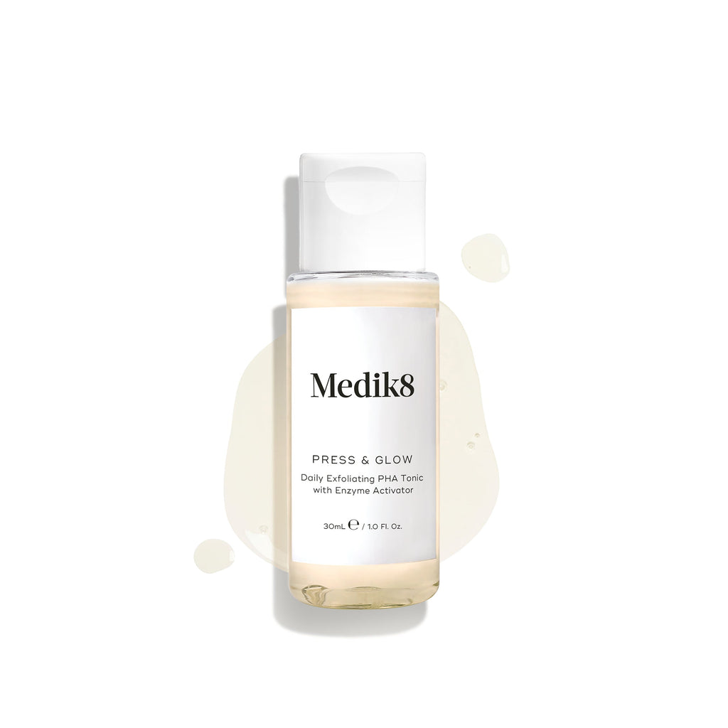 A 30ml/1.0 fl. oz bottle of Medik8 Press & Glow™ (Travel Size) Daily Exfoliating PHA Tonic with Enzyme Activator for sensitive skin, featuring a light splash behind it.
