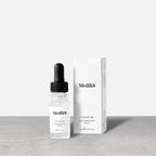A Medik8 Hydr8 B5™ Liquid Rehydration Serum, equipped with a dropper and enriched with hyaluronic acid for superior skin hydration, is positioned next to its white packaging on a gray surface against a plain background.
