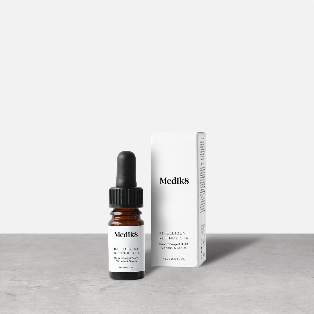 A bottle of Medik8 Intelligent Retinol™ serum with a dropper rests next to its white packaging on a gray surface.