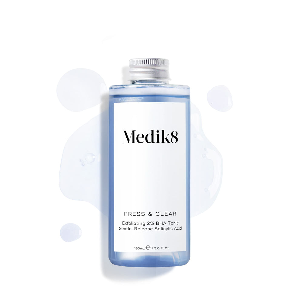 The Medik8 Press & Clear Refill™ Exfoliating 2% BHA Tonic, containing Salicylic Acid, is displayed on a white background with strategically spilled liquid around it.