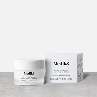 A jar and box of Medik8 Total Moisture Daily Facial Cream™ are displayed on a light gray surface, highlighting daily moisturizing benefits and skin barrier support against a plain background.