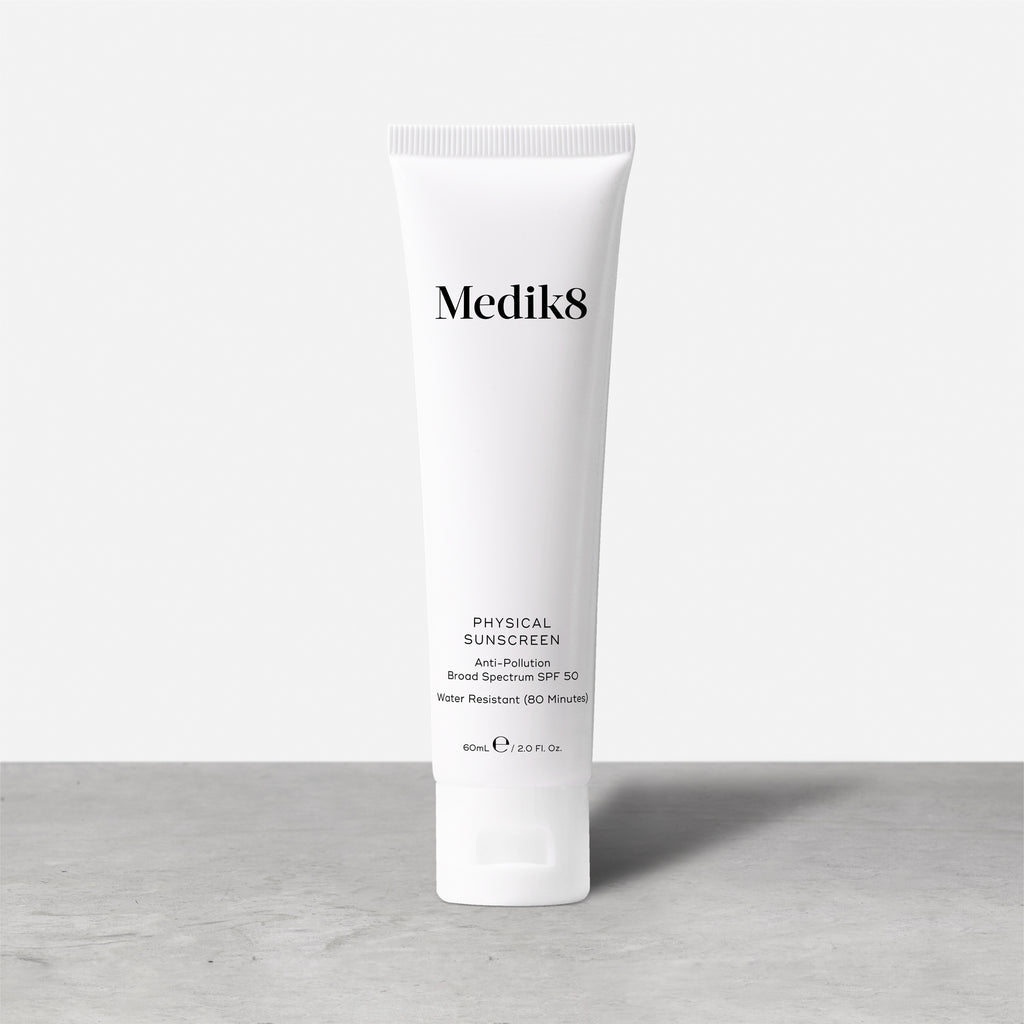 The Medik8 Physical Sunscreen™ in a 60ml white tube offers SPF50 with UVA/UVB protection and anti-pollution benefits, standing sleekly on a gray surface against a light gray background.